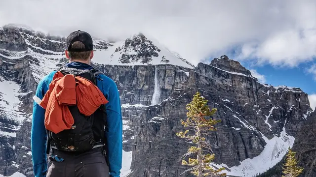A hiker watches an avalanche release on a snow-loaded cliff face.