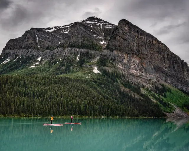 Two paddleboarders on the turquoise water of Lake Louise with Fairview Mountain rising above the far shore.